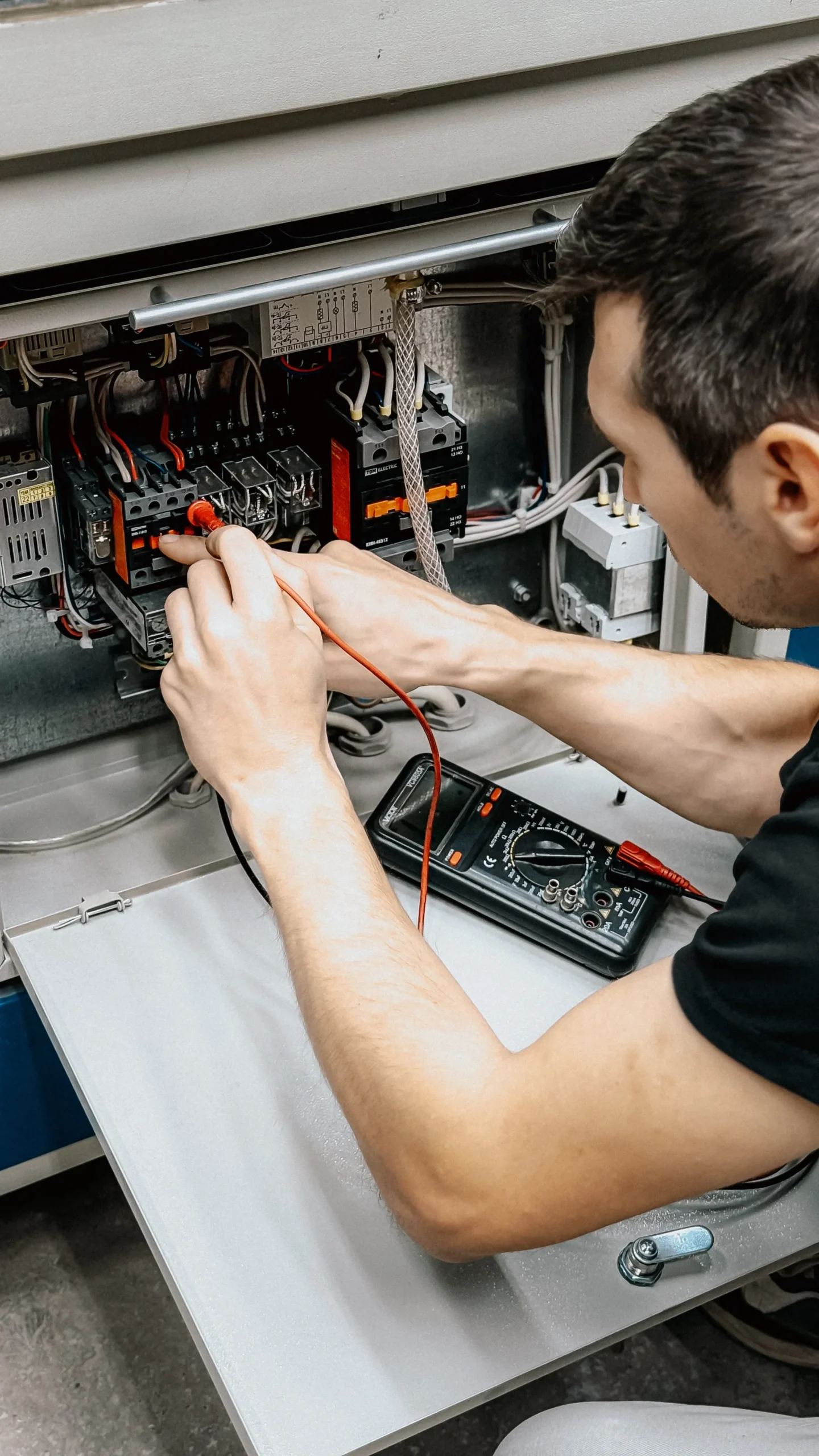 Male electrician testing an electrical panel with a multimeter during fault diagnosis
