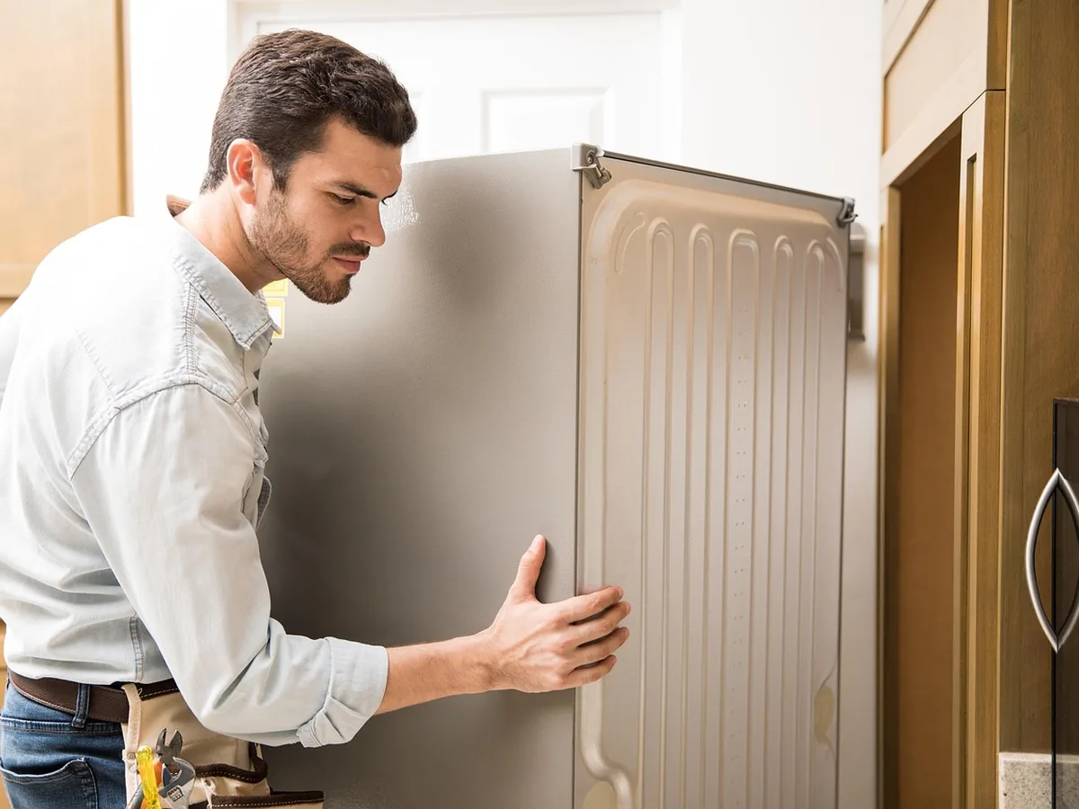 Male technician positioning a refrigerator to inspect its rear and side access