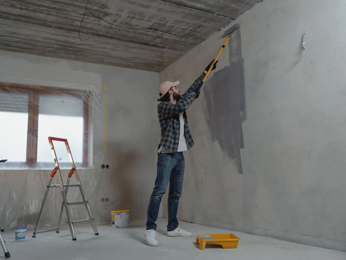Male painter applying paint to an interior wall with a roller in a protected room