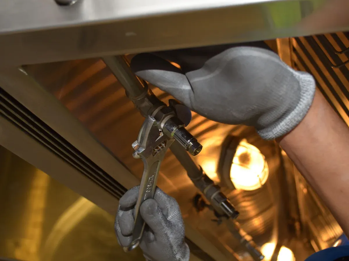 Gloved technician tightening a plumbing connection with a wrench