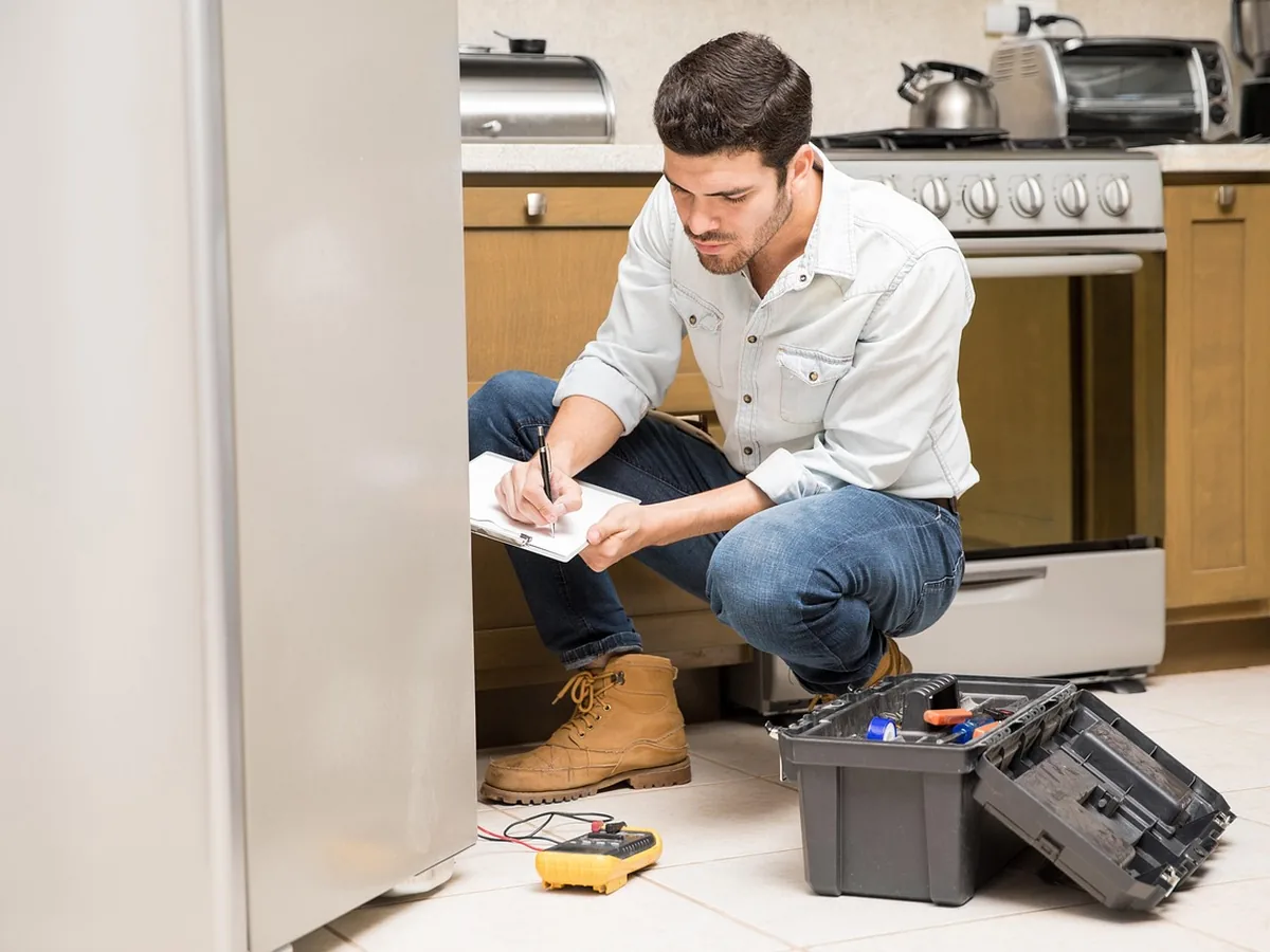 Male refrigerator technician inspecting a fridge with tools in a kitchen