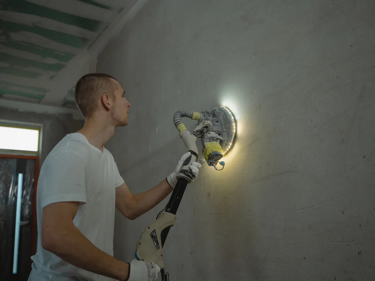 Male worker sanding an interior wall as part of surface preparation before painting